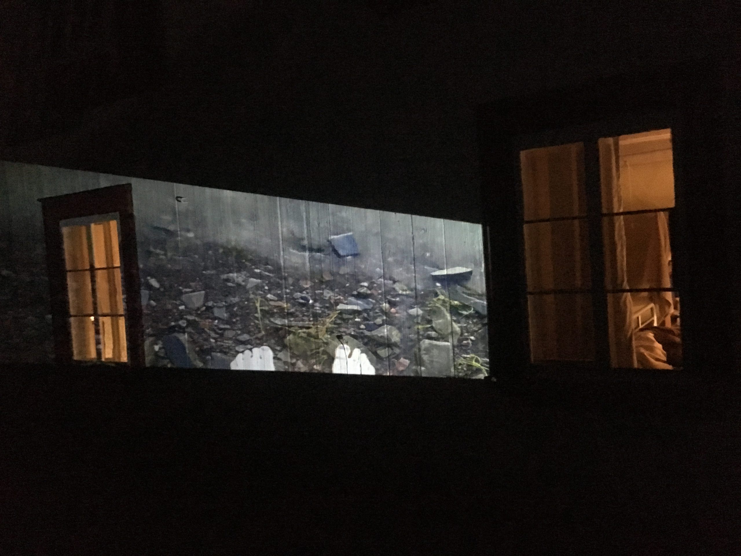 La vidéo captant les pieds de l'artiste dans le fleuve est projetée sur le mur extérieur d'une maison.