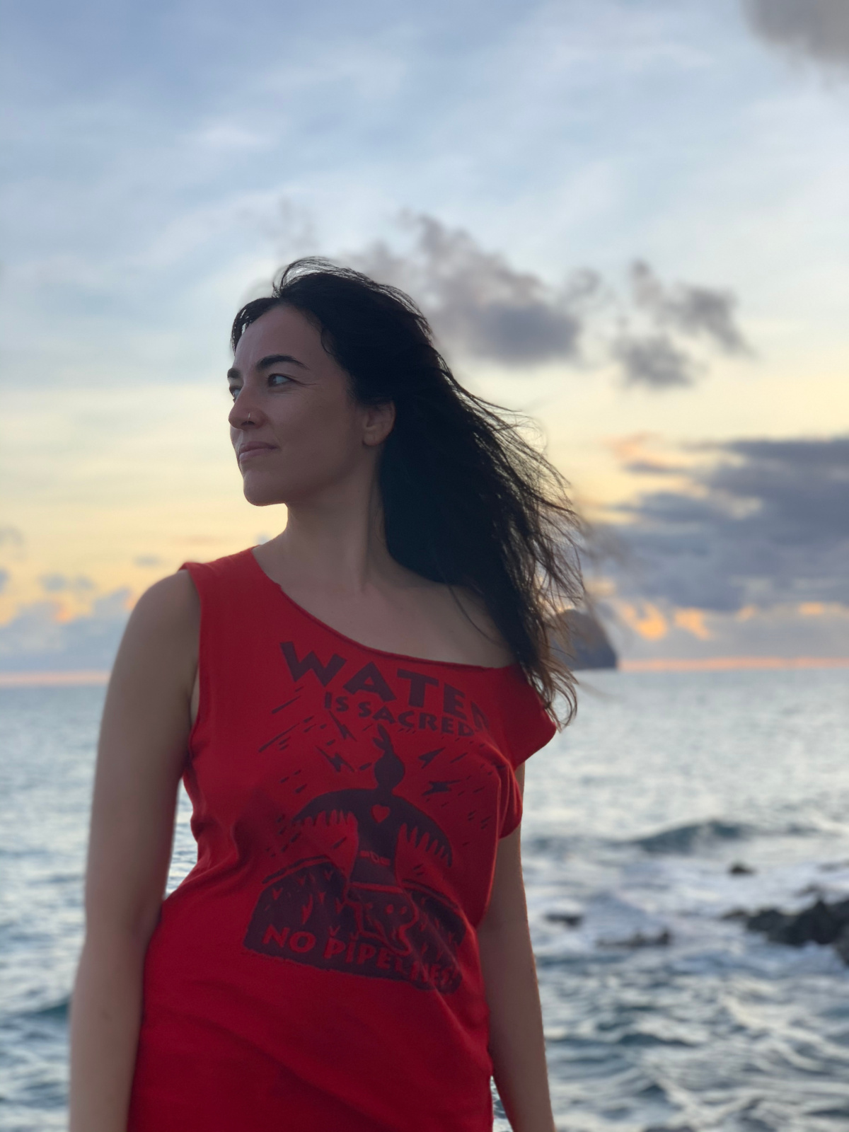 Émilie Monnet sur la plage en Martinique. Elle porte un t-shirt rouge sur lequel il est écrit «Water Is Sacred» (L'eau est sacrée). 